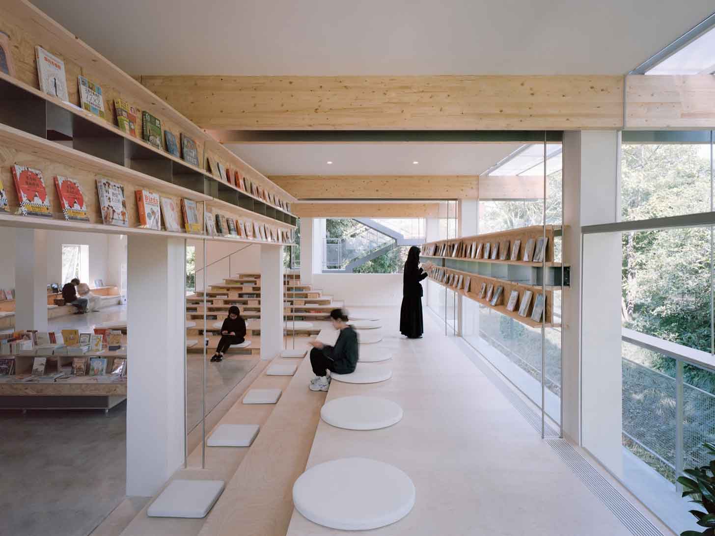 Two bookstore visitors look at shelves, which overlook big windows out into nature