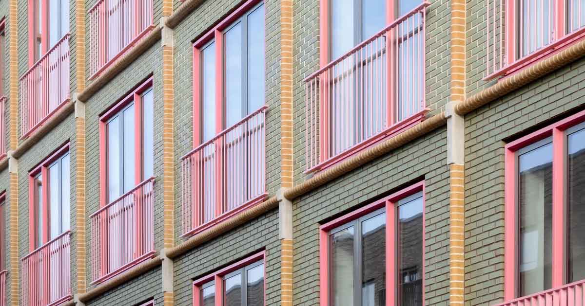 A closeup of a building with sage green, bubblegum pink, and yellow brick details 