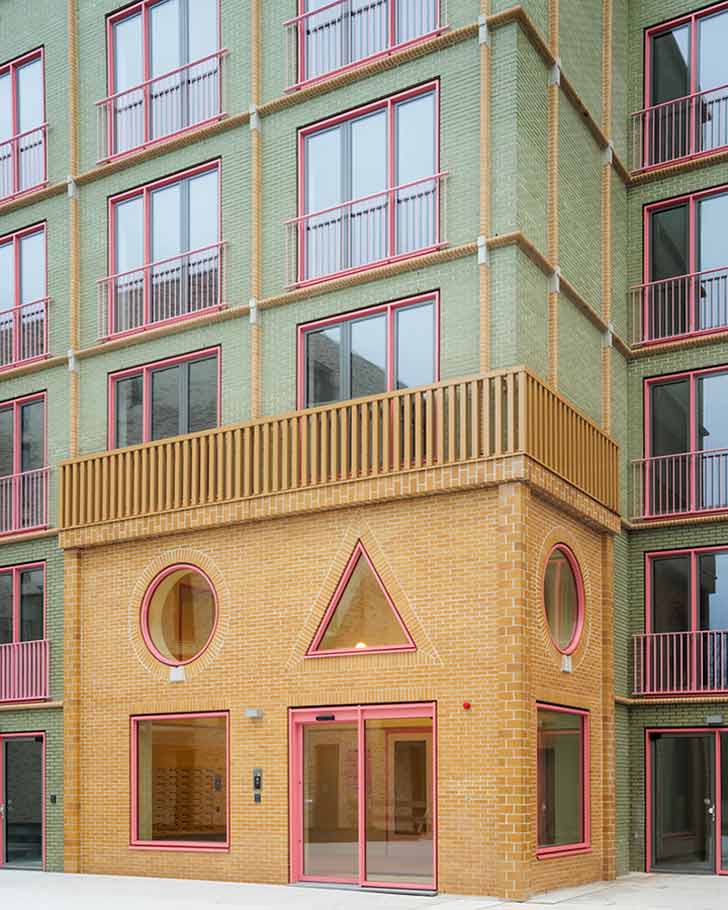 A green brick building with a yellow brick entrance, complete with circular and triangular windows