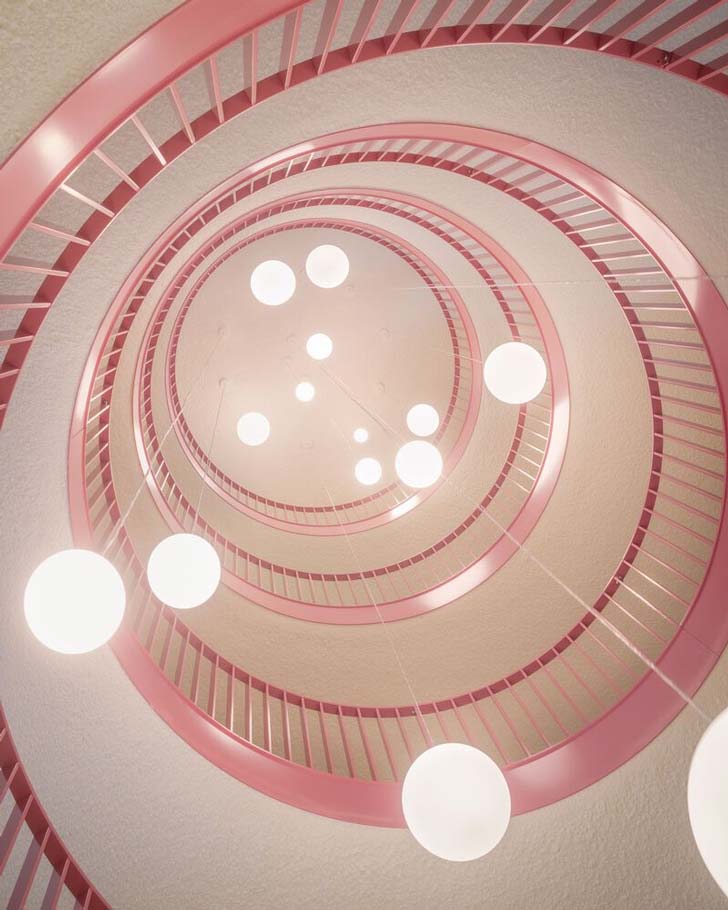 An upward angle of a pink staircase with spherical light fixtures