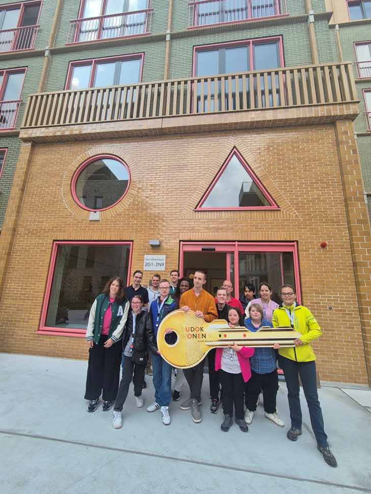 A group of young people stand in front of their new apartment building with a large cutout of a key