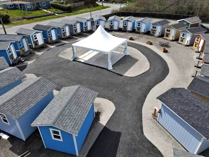 A circular community of tiny homes, built facing a white tent in the middle of the community sqaure