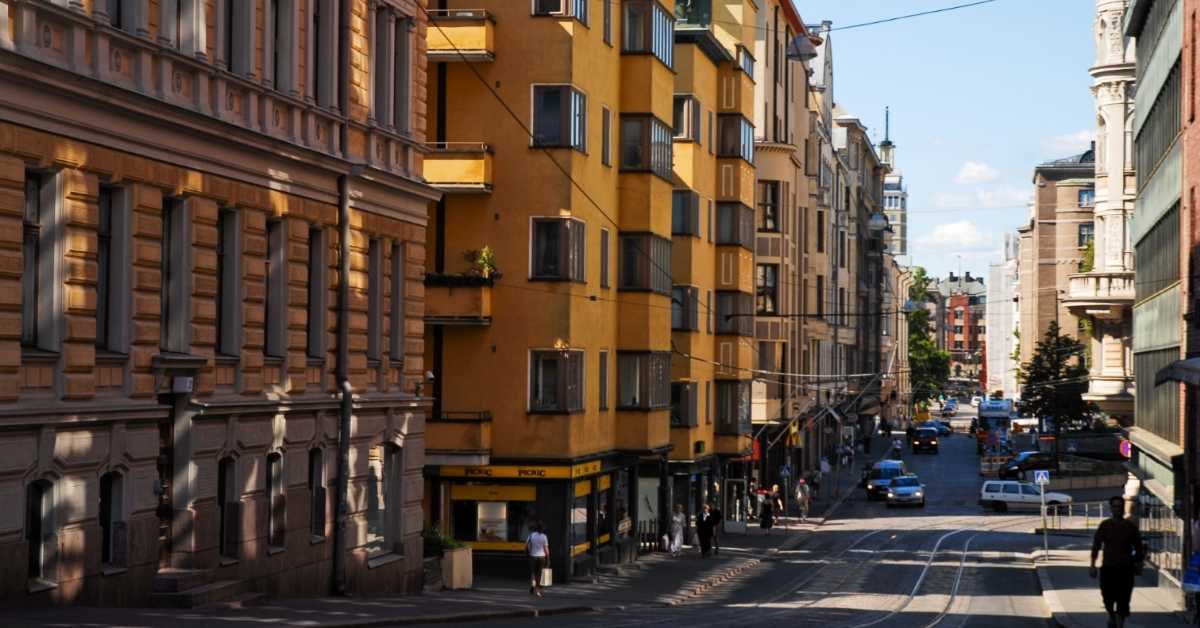 A zoomed out shot of a city street in Helsinki, Finland. It is daytime and the road is sparse with cars and people. 