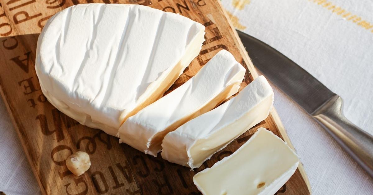 A charcuterie board with a white brie cut into pieces across the top. 