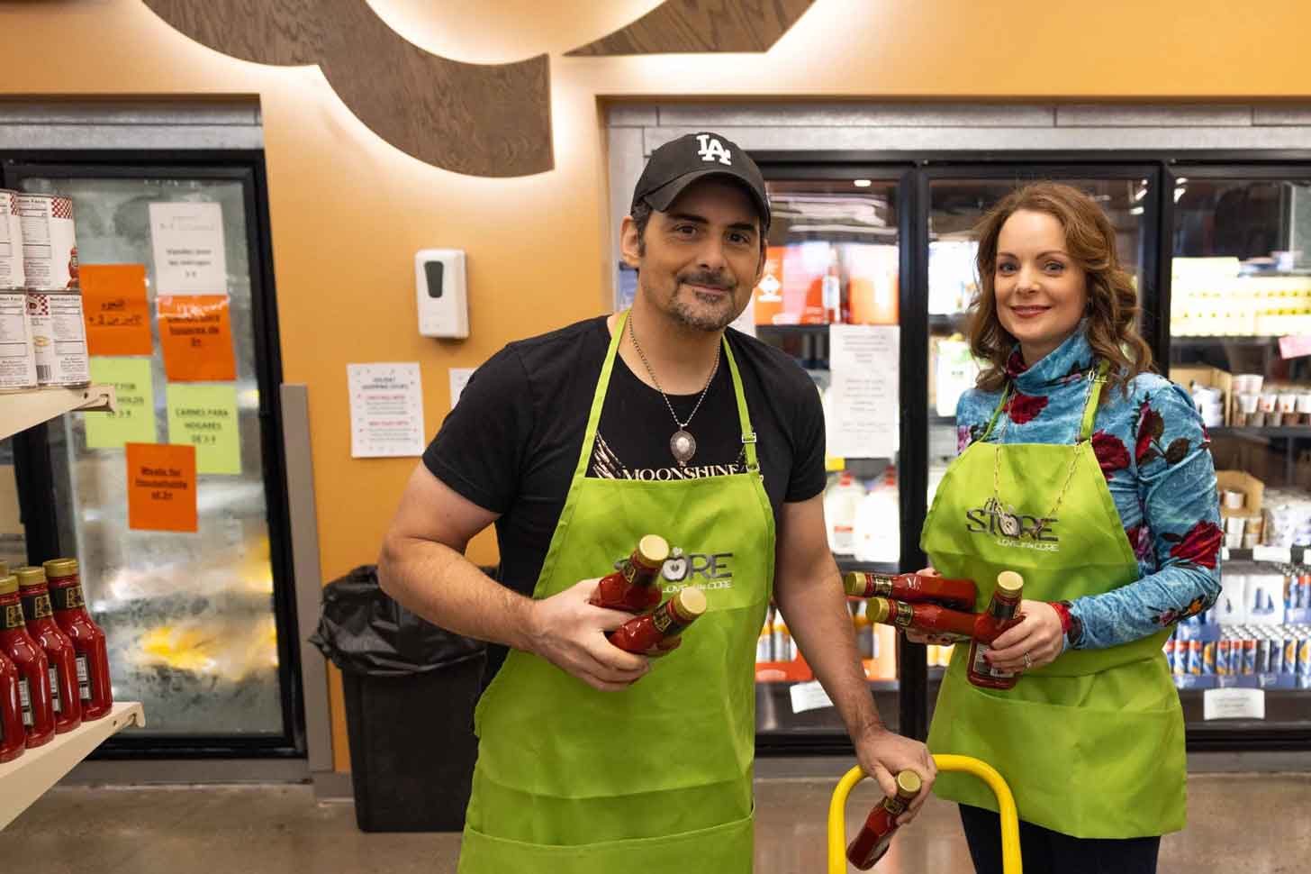 Brad Paisley and Kimberly Williams-Paisley wear green aprons in a grocery store