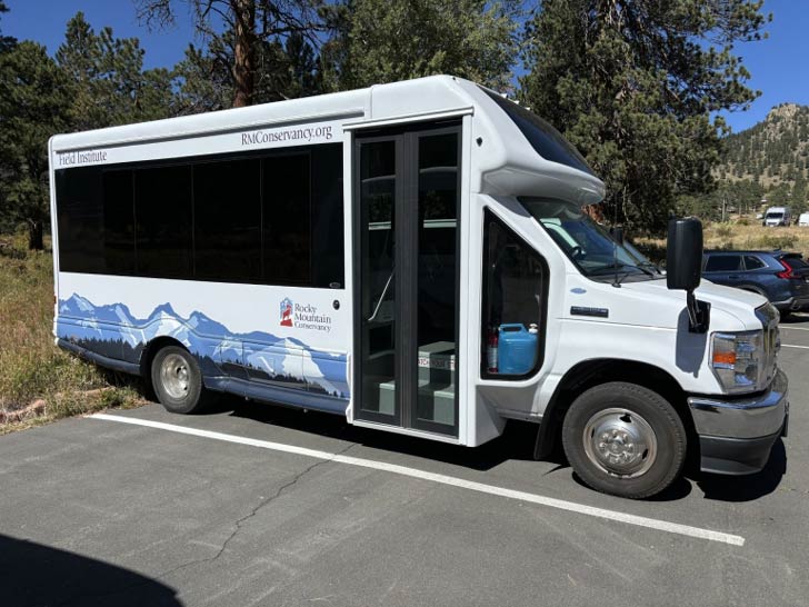 A white bus sits in a parking lot at Rocky Mountain National Park
