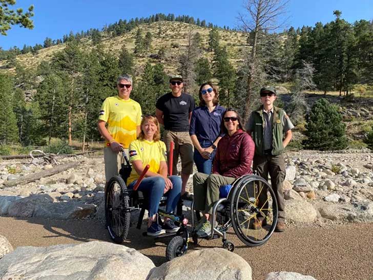 Six people, two in wheelchairs, pose together, smiling, in Rocky Mountain National Park