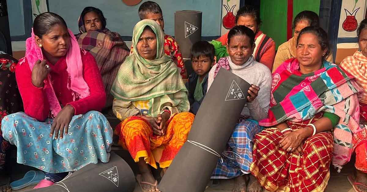 A group of Nepalese women in girls in brightly colored clothing hold rolled-up black rubber mats