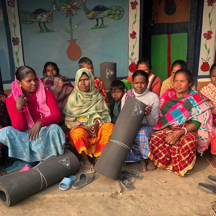 A group of Nepalese women in girls in brightly colored clothing hold rolled-up black rubber mats