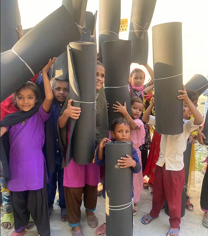 A group of Nepalese children holds up rolled black rubber mats, smiling