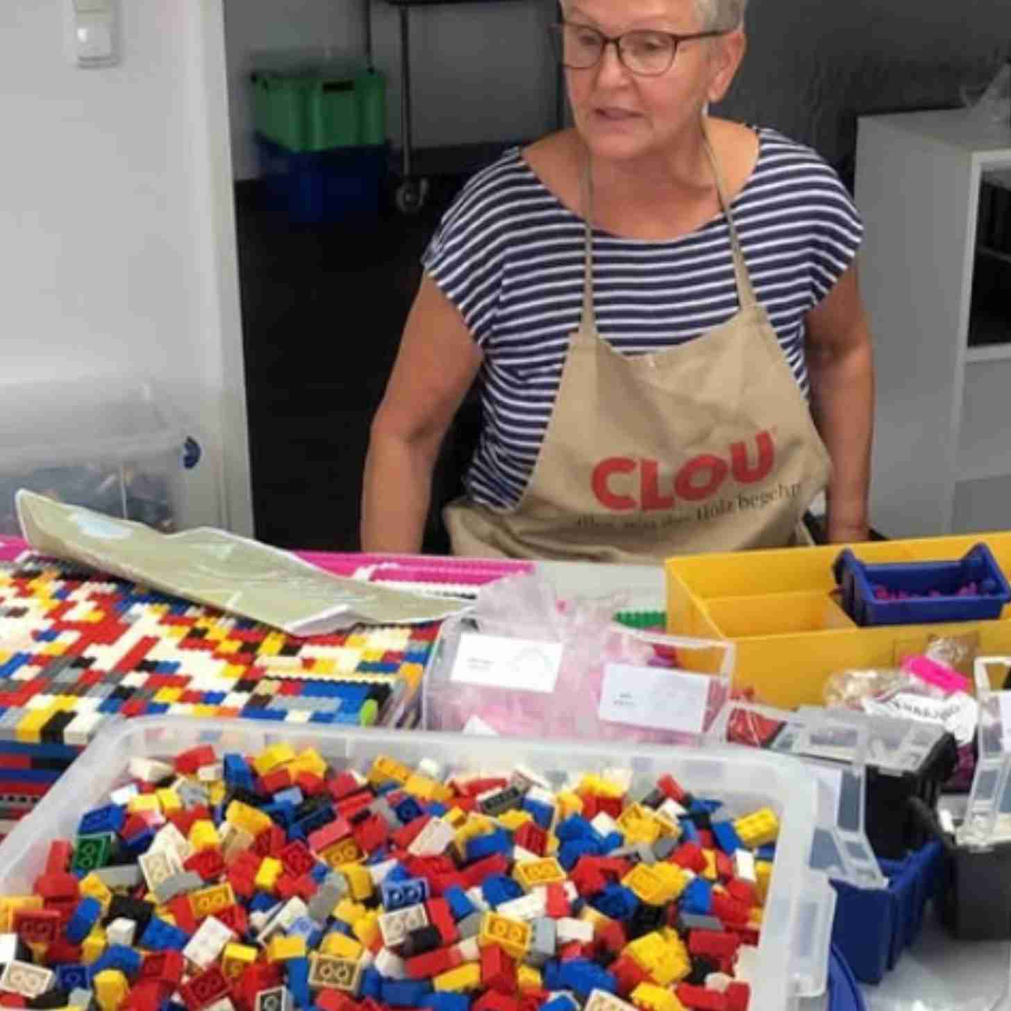 an elderly woman looks around her kitchen counter, which is covered in buckets of legos