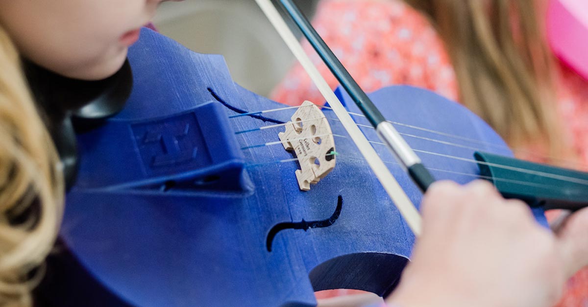 A close-up of a child playing a blue 3D printed violin