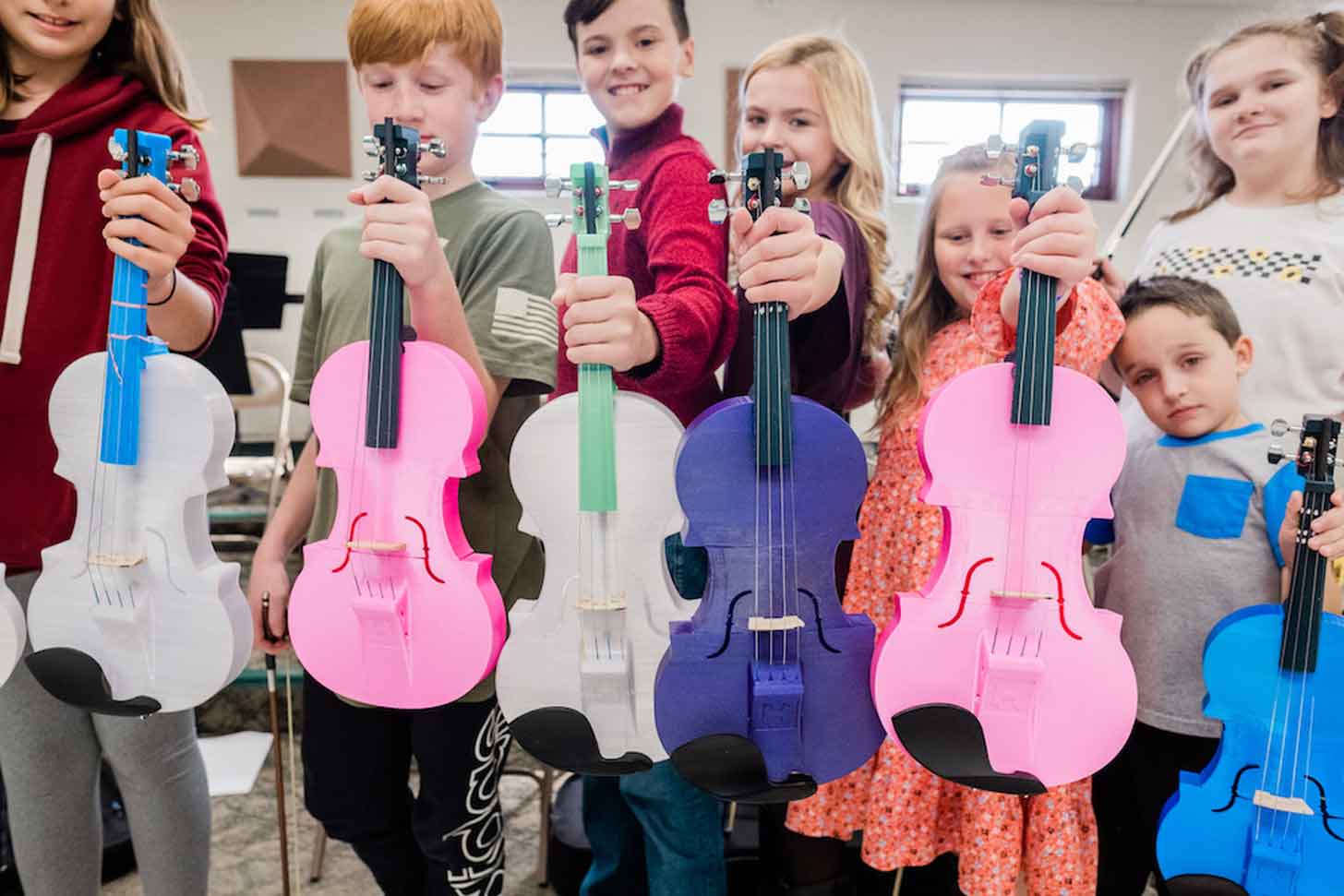 A close-up of 7 elementary schoolers holding up colorful violins