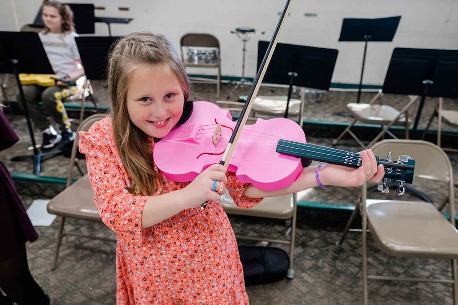 A young girl plays a pink violin in elementary school