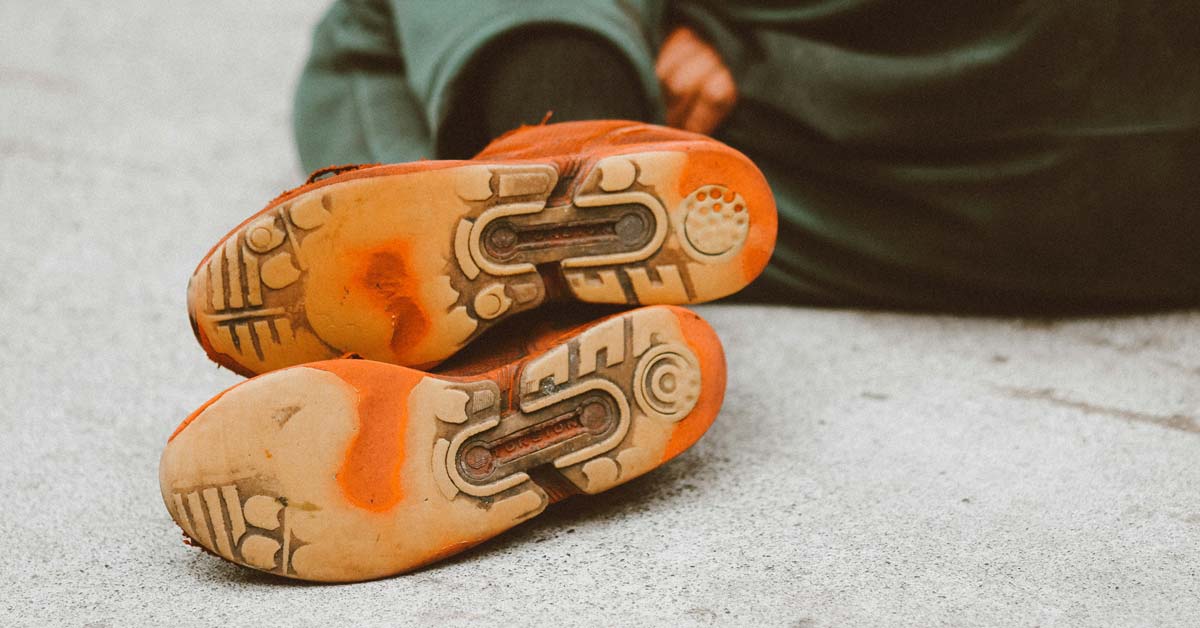 A close-up image of the bottom of a pair of worn-out orange sneakers on the feet of someone sleeping on the ground