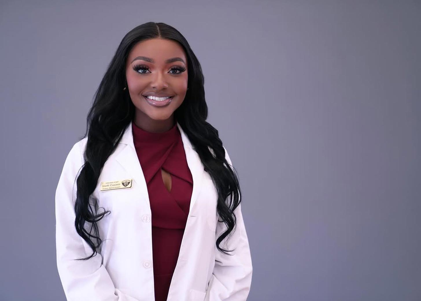 A young Black woman in a white doctor's coat with a maroon blouse underneath