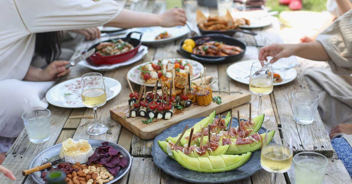 An aerial view of a picnic table full of food, with people's arms reaching over to grab a bite