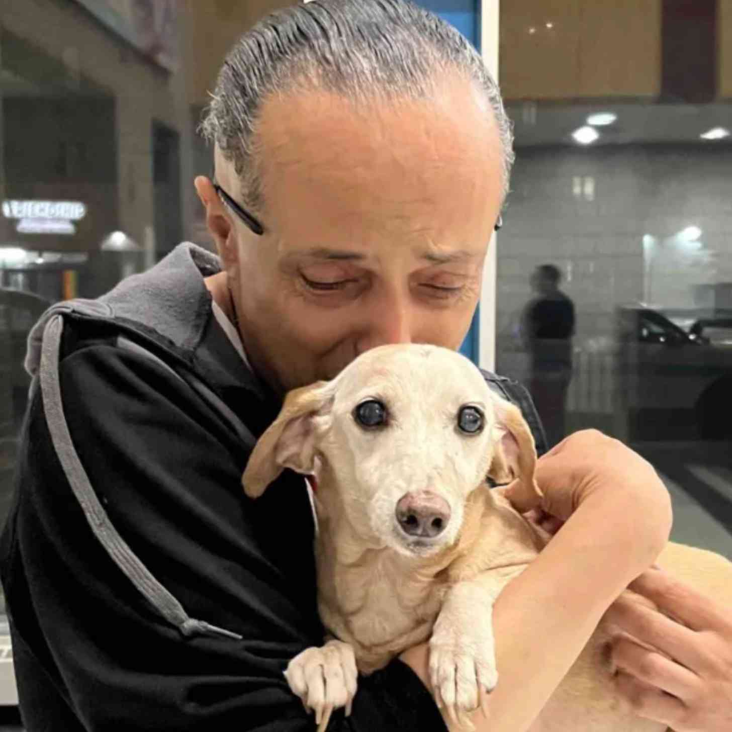 A man with thinning hair looks down as he tightly hugs a small dachshund.