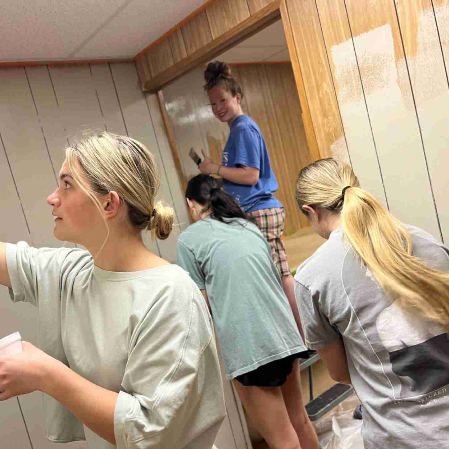 Several teen girls paint a room as they smile