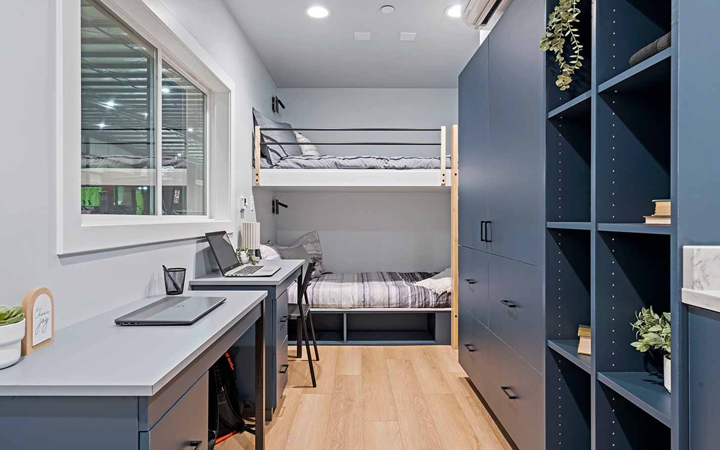 An interior view of a dorm room with two bunk beds, desks, and storage