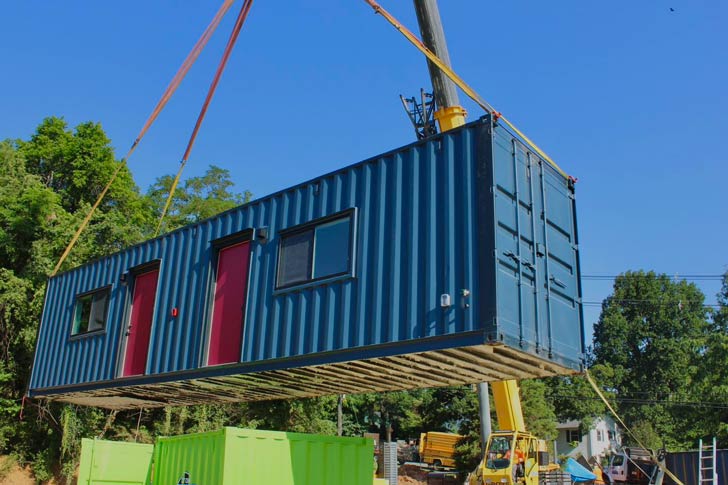 A blue and red shipping container home on a lift