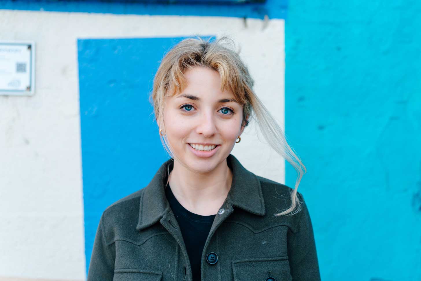 Kat Abughazaleh, a young woman with light skin and blond hair, in front of a blue wall