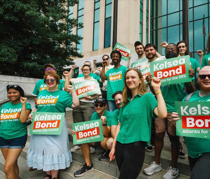 A community of diverse people gathers around Kelsea Bond, a candidate for Atlanta City Council. They hold up green signs that read: Kelsea Bond: Atlanta for the 99%"