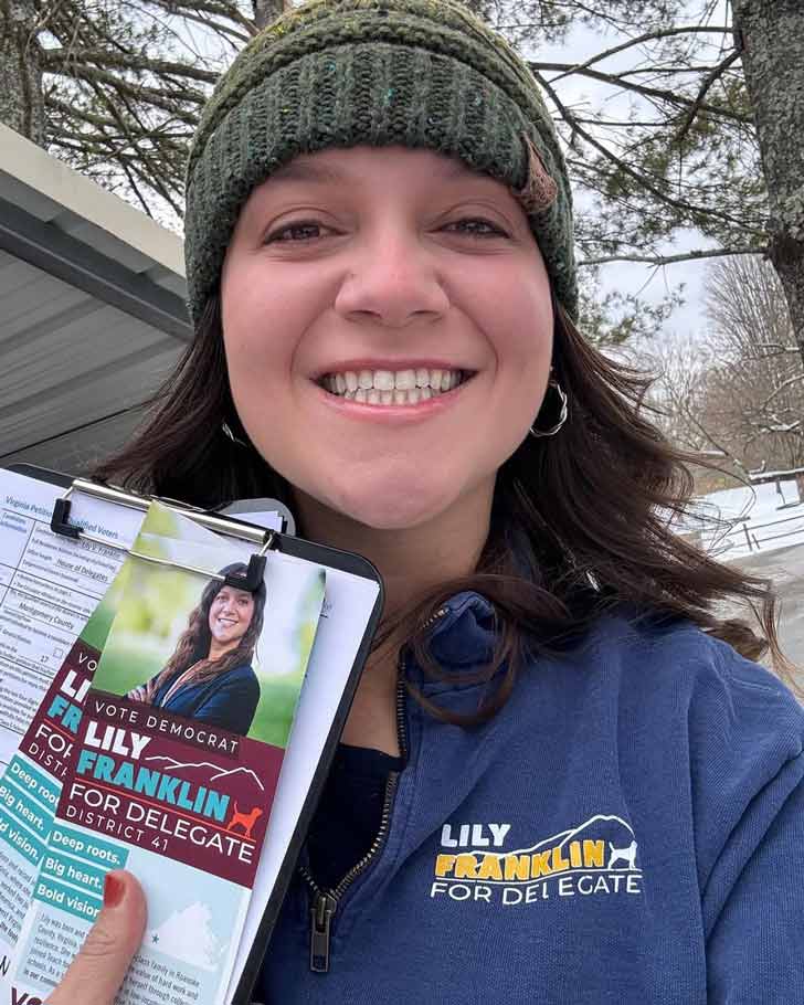 A young white woman with brunette hair holds up a pamphlet for her state assembly candidacy.