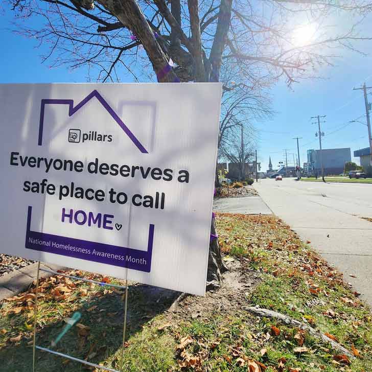 A white yard sign with a purple house that reads " Everyone deserves a safe place to call home."