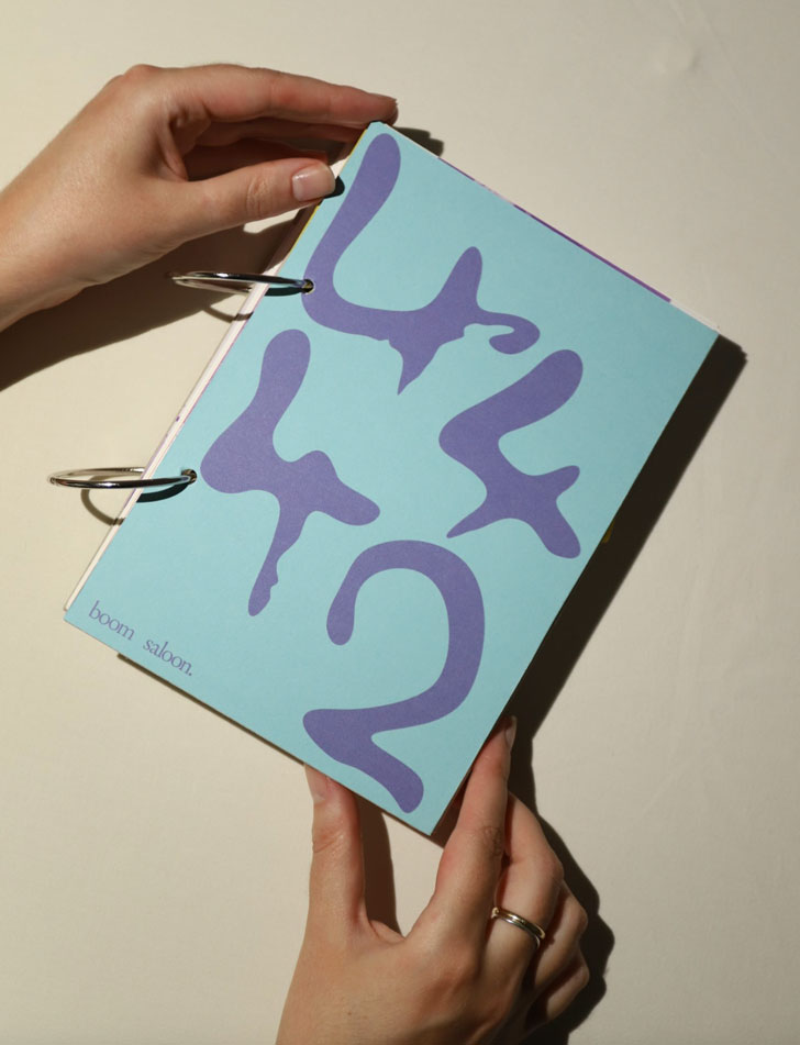 Two hands hold up a metal ring-bound book that is blue with purple numbers: 4442