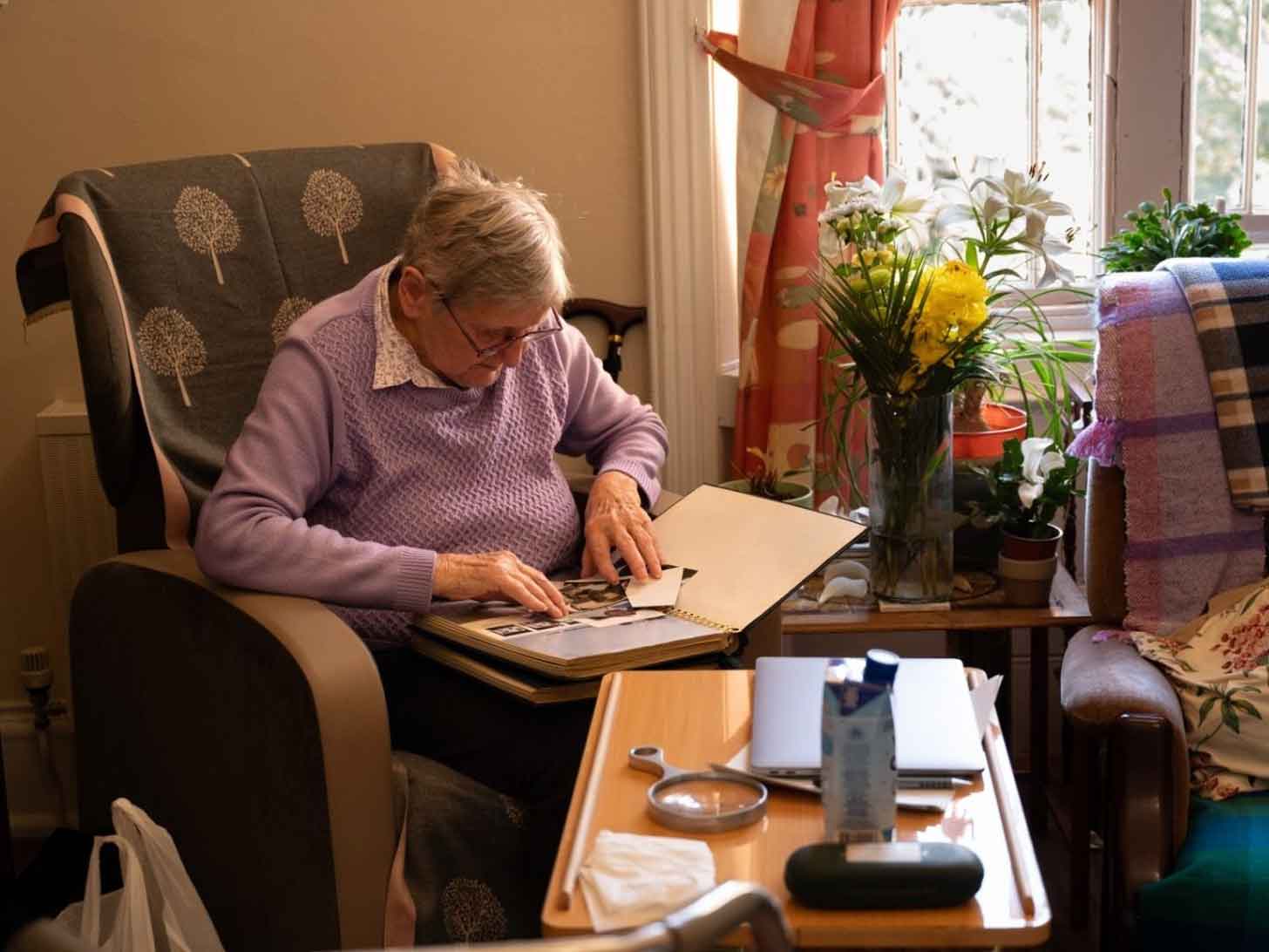 An old woman sits in a rocking chair and pieces together a scrapbook