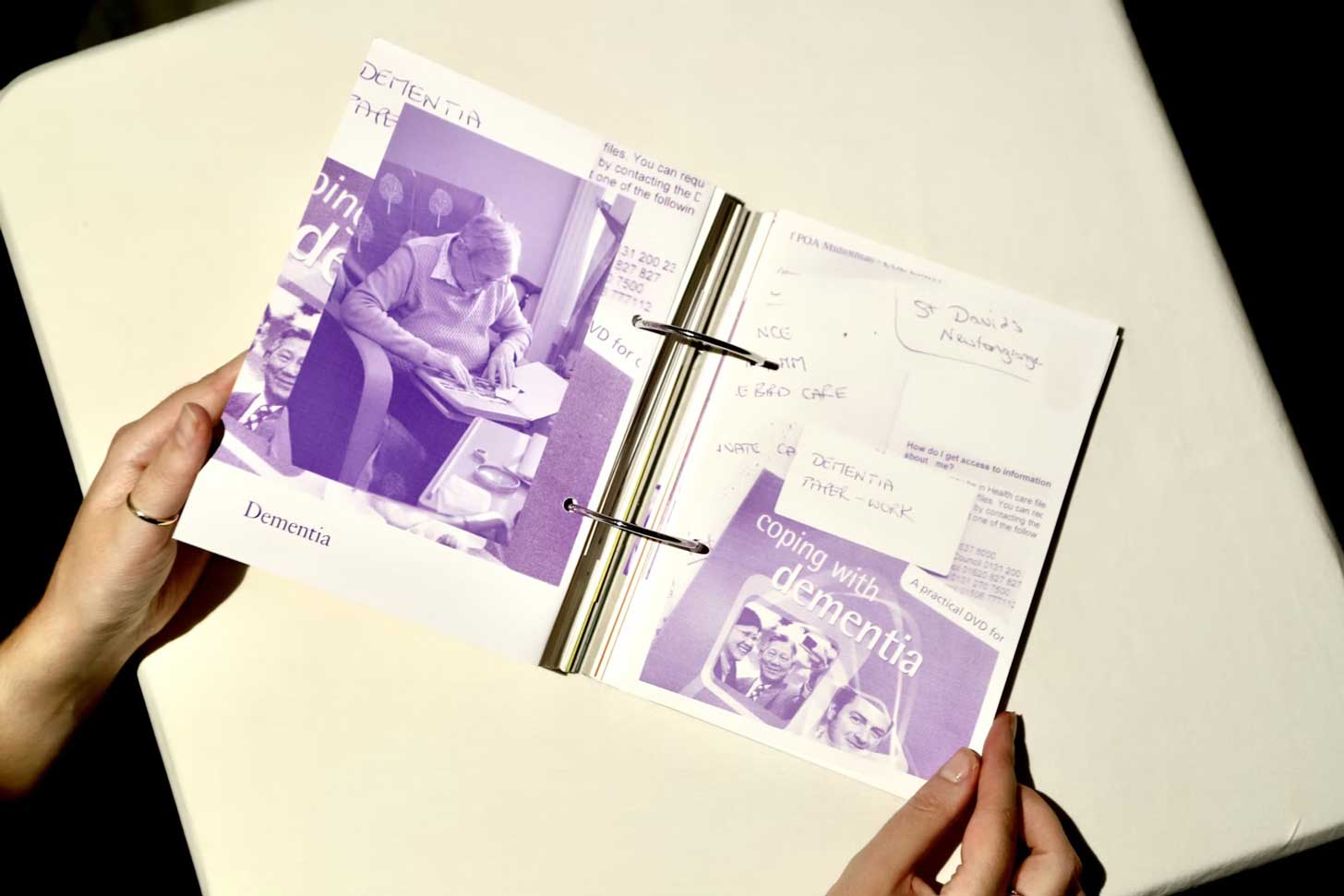 A flat-lay of a book secured by two silver rings. Inside is a monochrome purple collage of words and images relfecting dementia