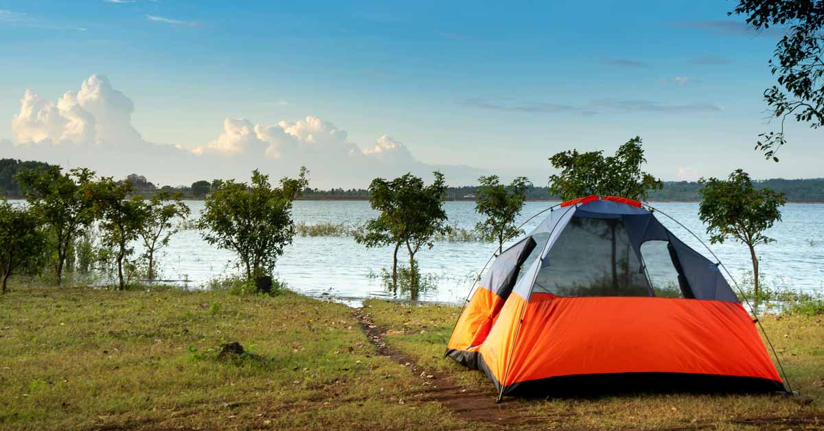 An orange tent sits on a grassy campsite next to a lake
