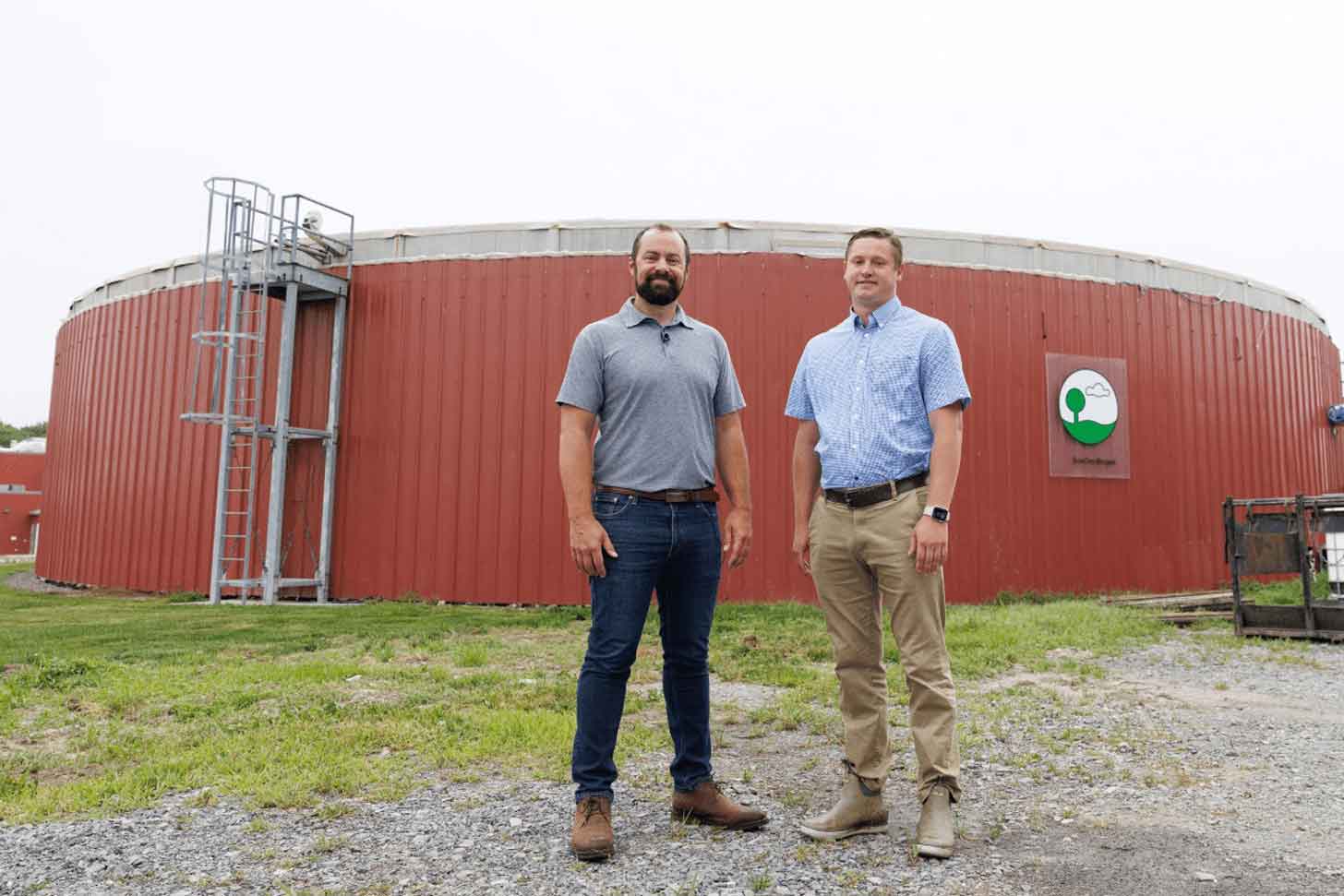 Two men stand outside a red farm digester