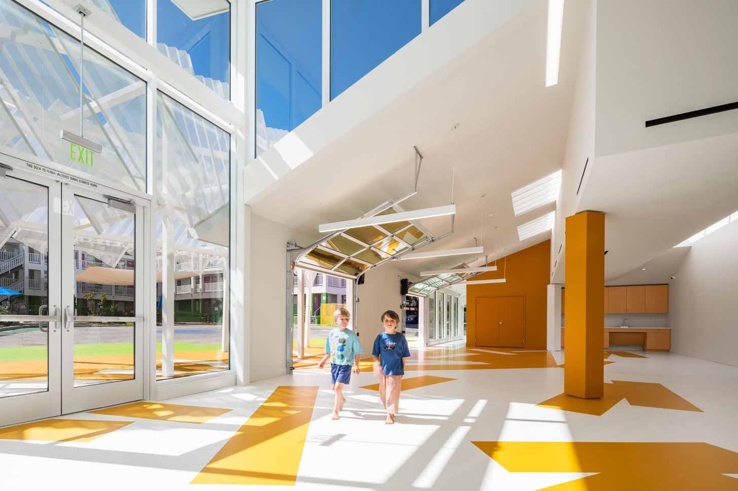 Two young boys walk through an open-concept community center with large windows pouring in natural light
