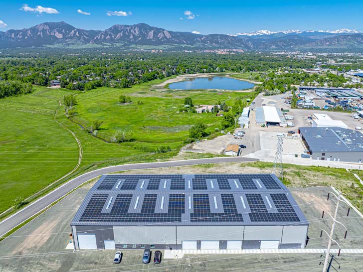 A solar powered factory sits in the foothills of Boulder, Colorado, with a lake and mountains visible in the background