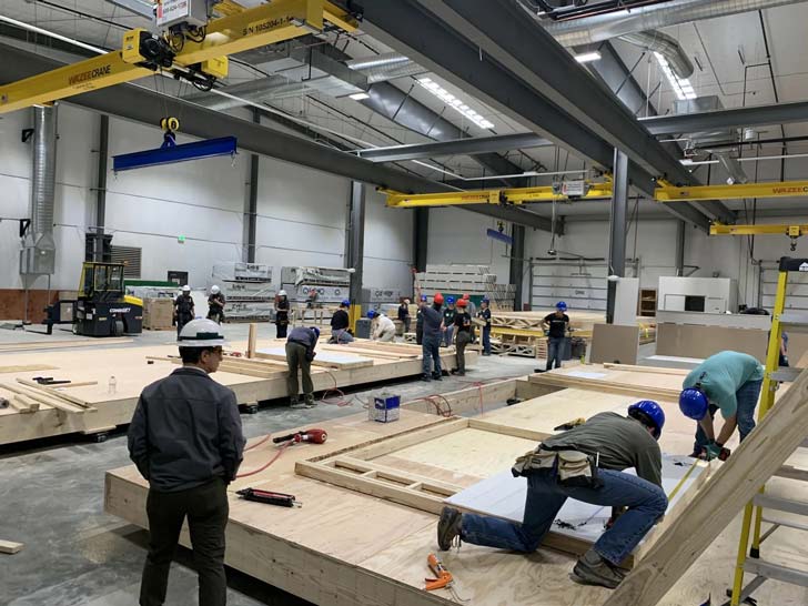 Students work on building the frames of prefab houses inside a factory