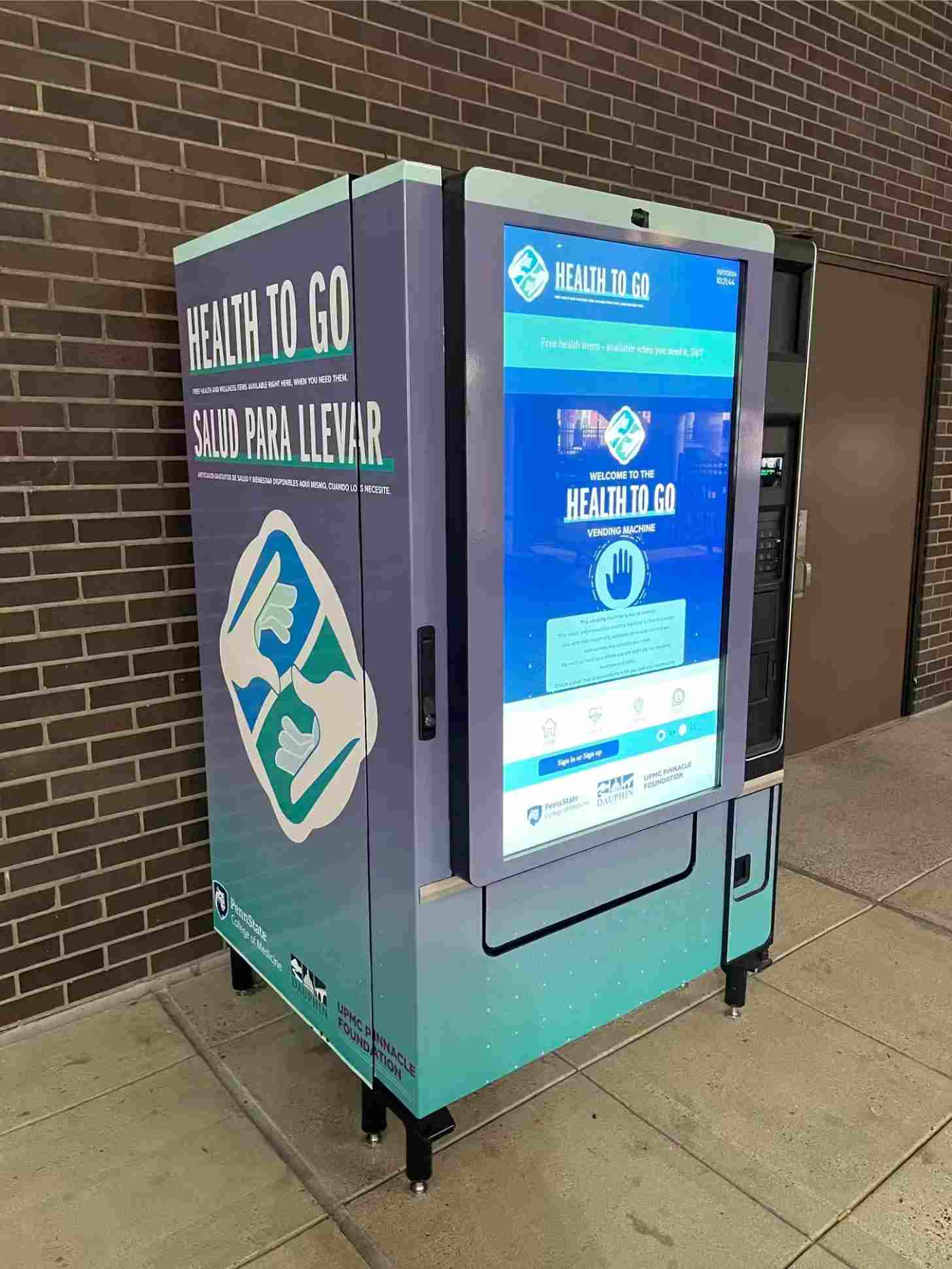A teal and grey vending machine that says 'Health To Go' with large digital touchscreen on front