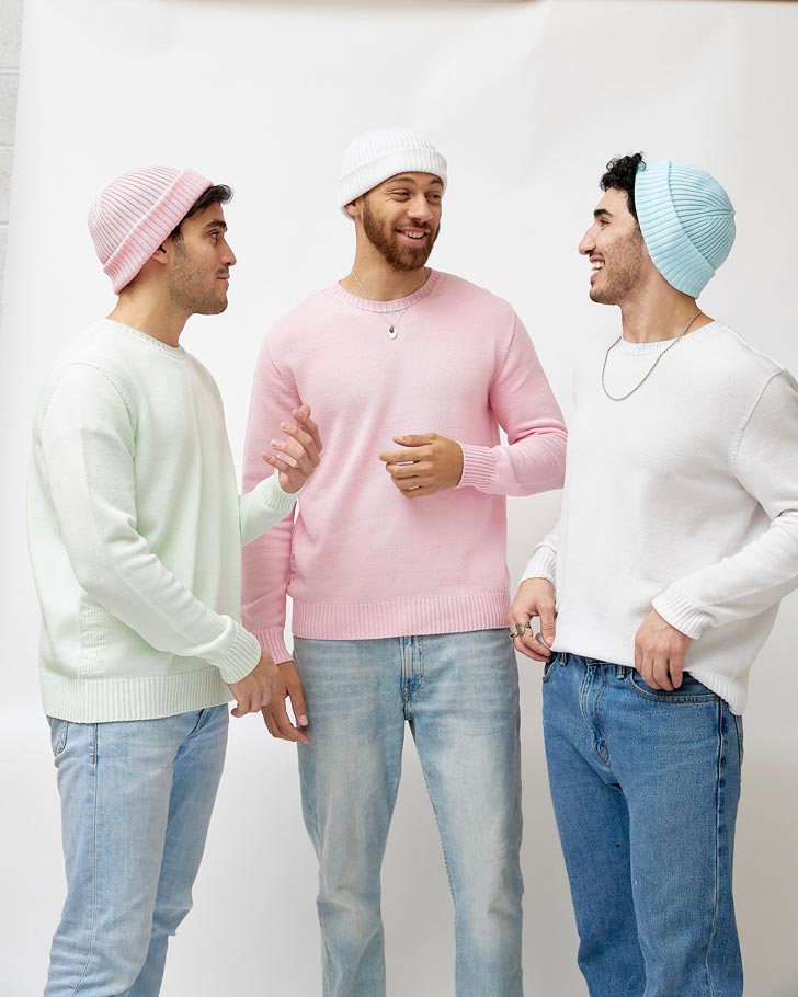 Three men wear pastel sweaters and knitted beanies against a white backdrop