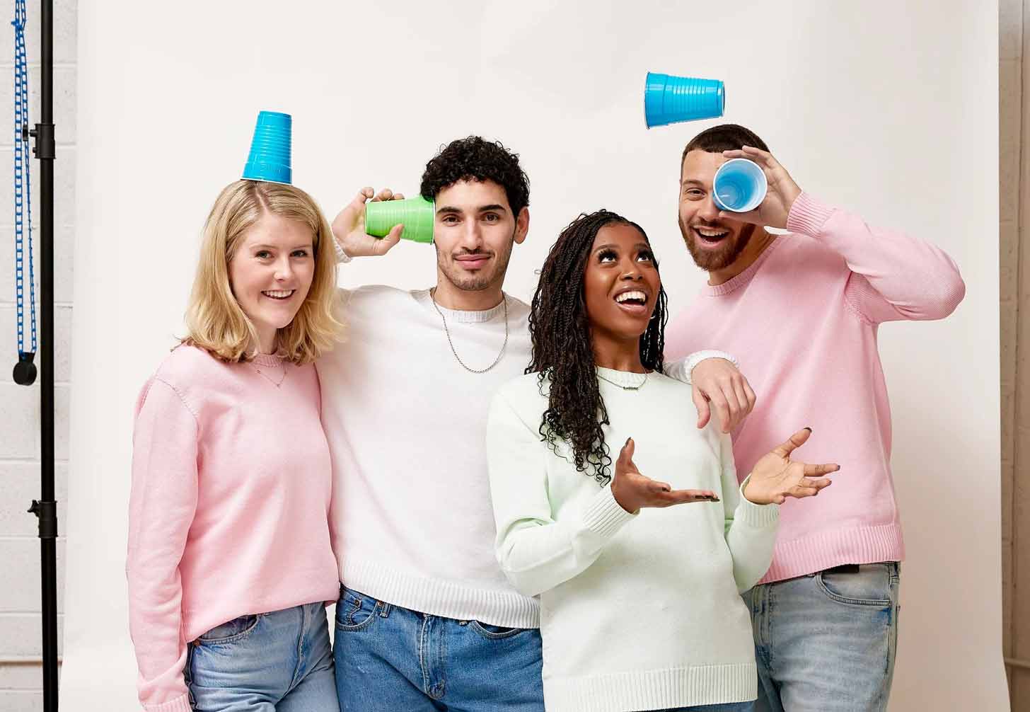 Two women and two men wear pastel sweaters and hold up colorful plastic party cups, smiling