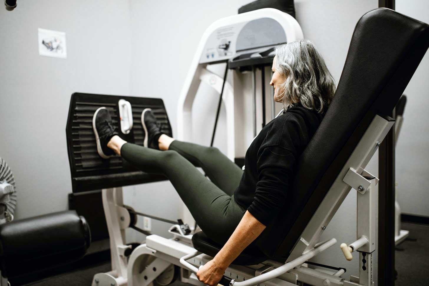A woman with gray hair sits in a leg press machine at the gym