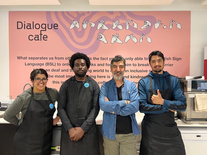 Four people stand side-by-side inside of a cafe run by deaf baristas