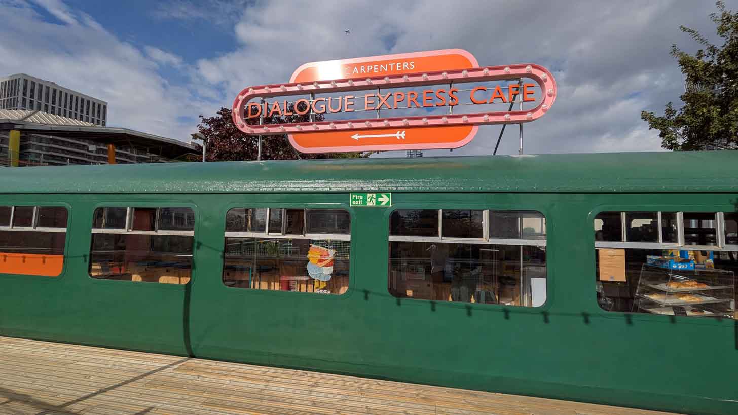 A green train carriage with an orange sign that reads Dialogue Express Cafe