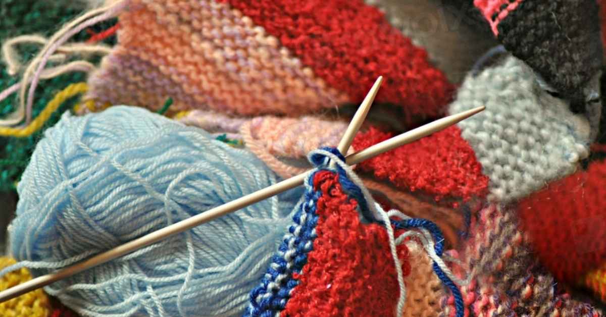 A pile of colorful knitting patterns, yarn, and yarnballs.