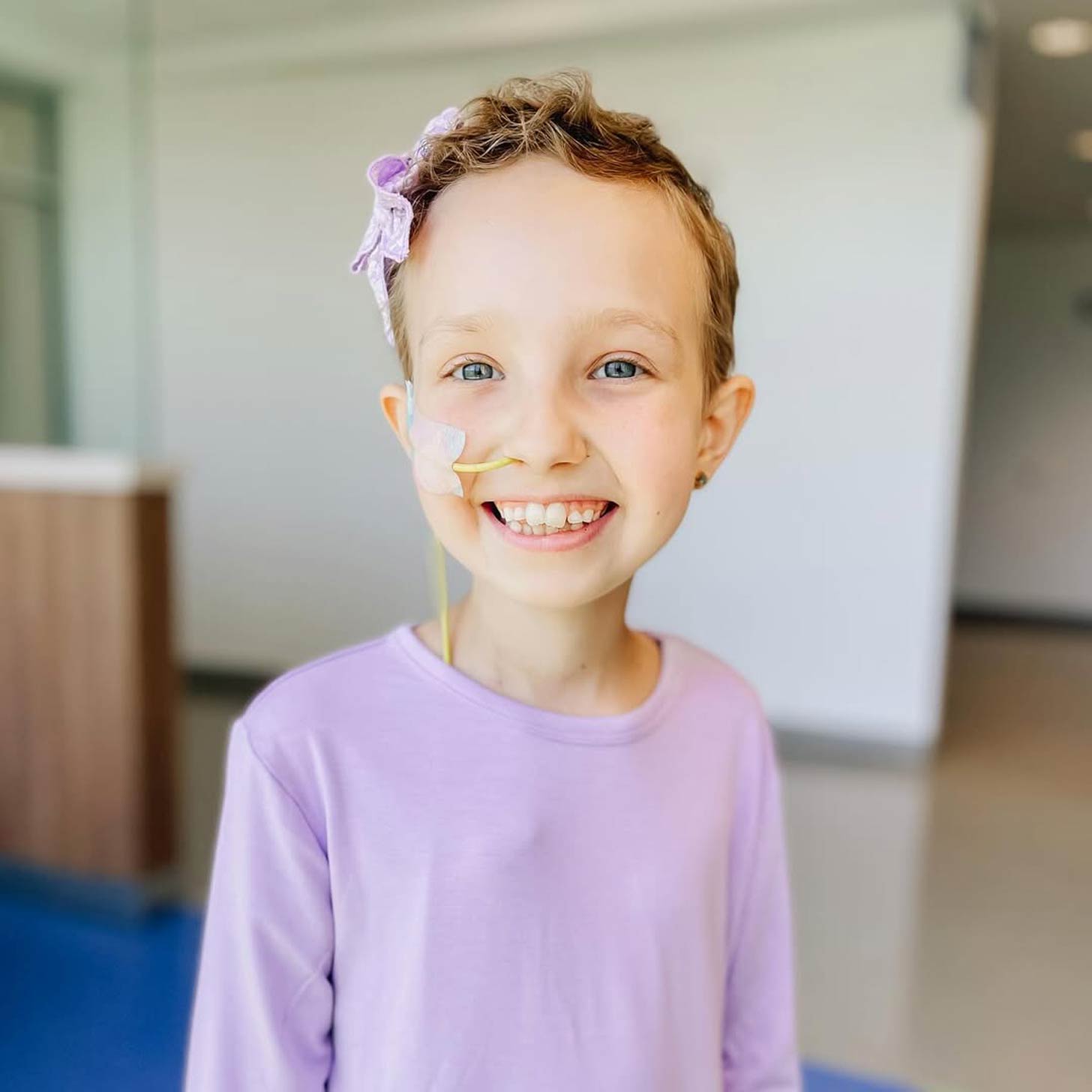 a 9-year-old girl with short blonde hair wearing a lavender shirt.