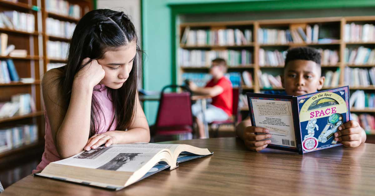 Two teens read at a table in a library