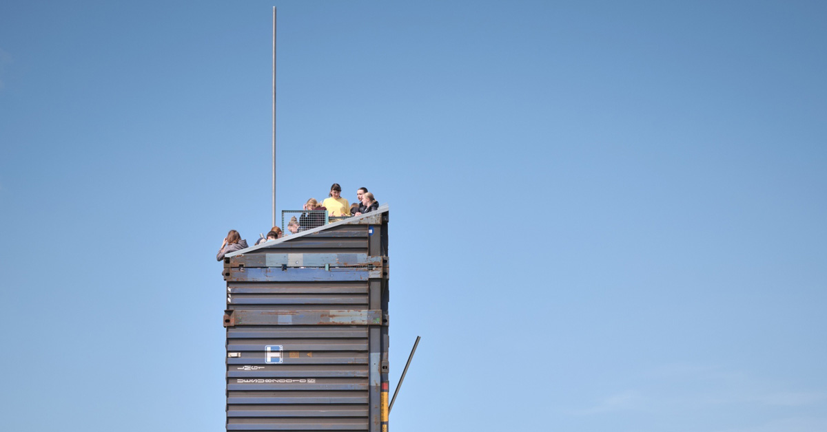 A closeup of tourists on the top of a lookout made from shipping containers
