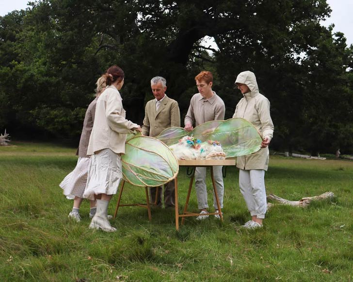A group of people enacts a burial ritual, surrounding a coffin made of seaweed wings
