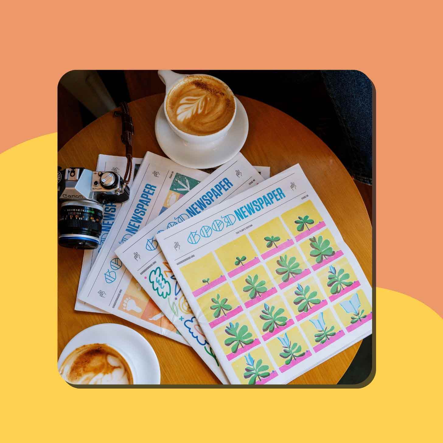 Four Goodnewspapers sit on a table next to a mug of coffee and a vintage film camera