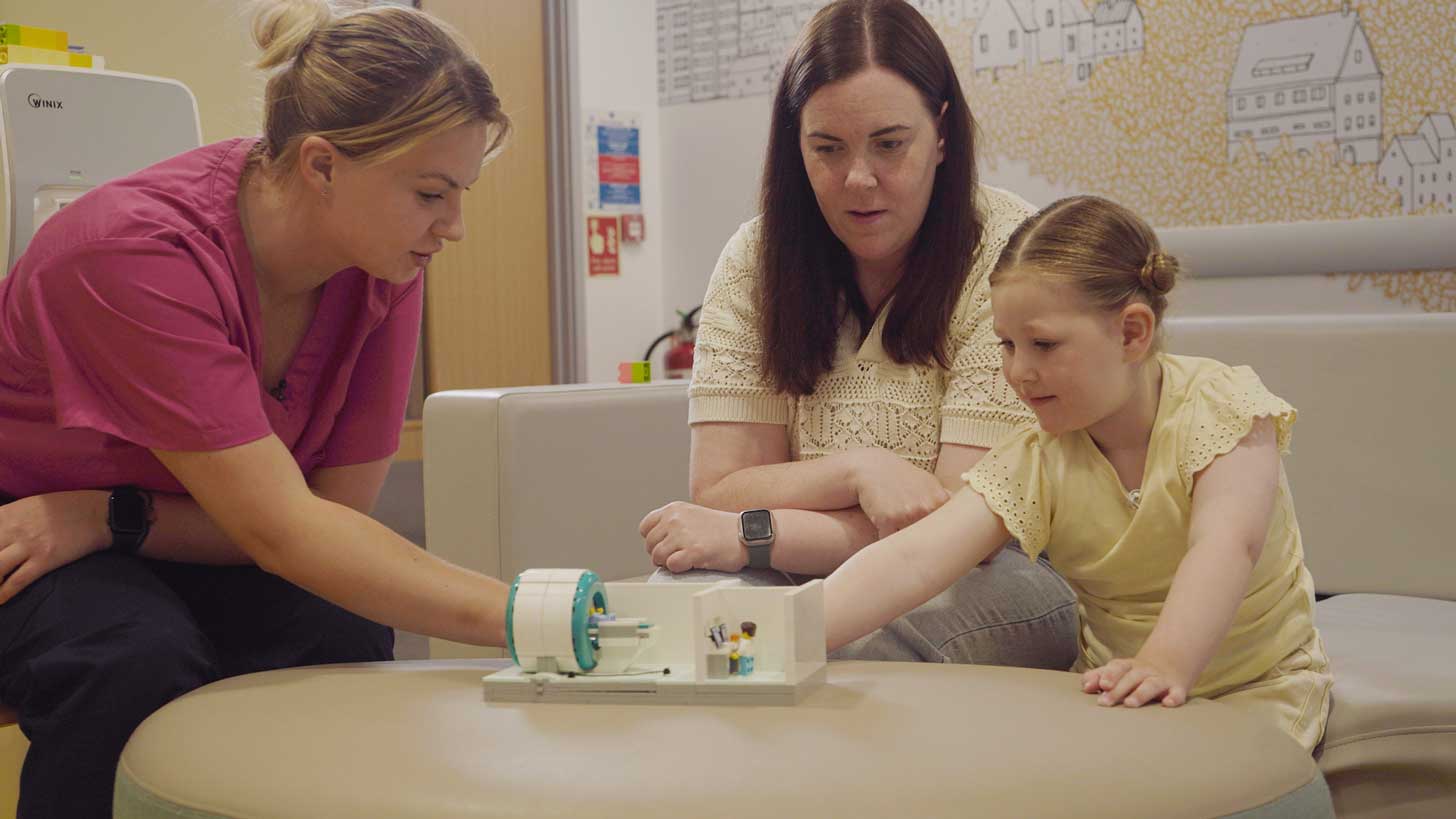 A young girl helps build a LEGO set with her mom and a healthcare professional